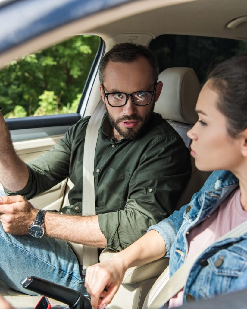teacher-pointing-on-something-to-student-in-car-during-driving-test-e1627375421688.jpg
